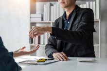 Person handing keys to outstreched hand. There is a minature toy car on the table.